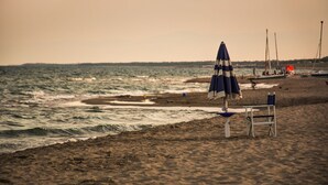 A beach with a row of beach chairs and a blue umbrella, a boat in the background, and a calm sea. - Trilocale - Two Bedroom Apartment, Sleeps 6 (Castellaneta)