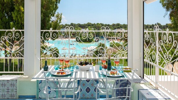 A terrace with a table set for dining, overlooking a pool and lush greenery. - Trilocale - Two Bedroom Apartment, Sleeps 6 (Castellaneta)