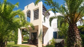 A modern house with a covered patio, surrounded by palm trees and a well-maintained lawn. - Trilocale - Two Bedroom Apartment, Sleeps 6 (Castellaneta)