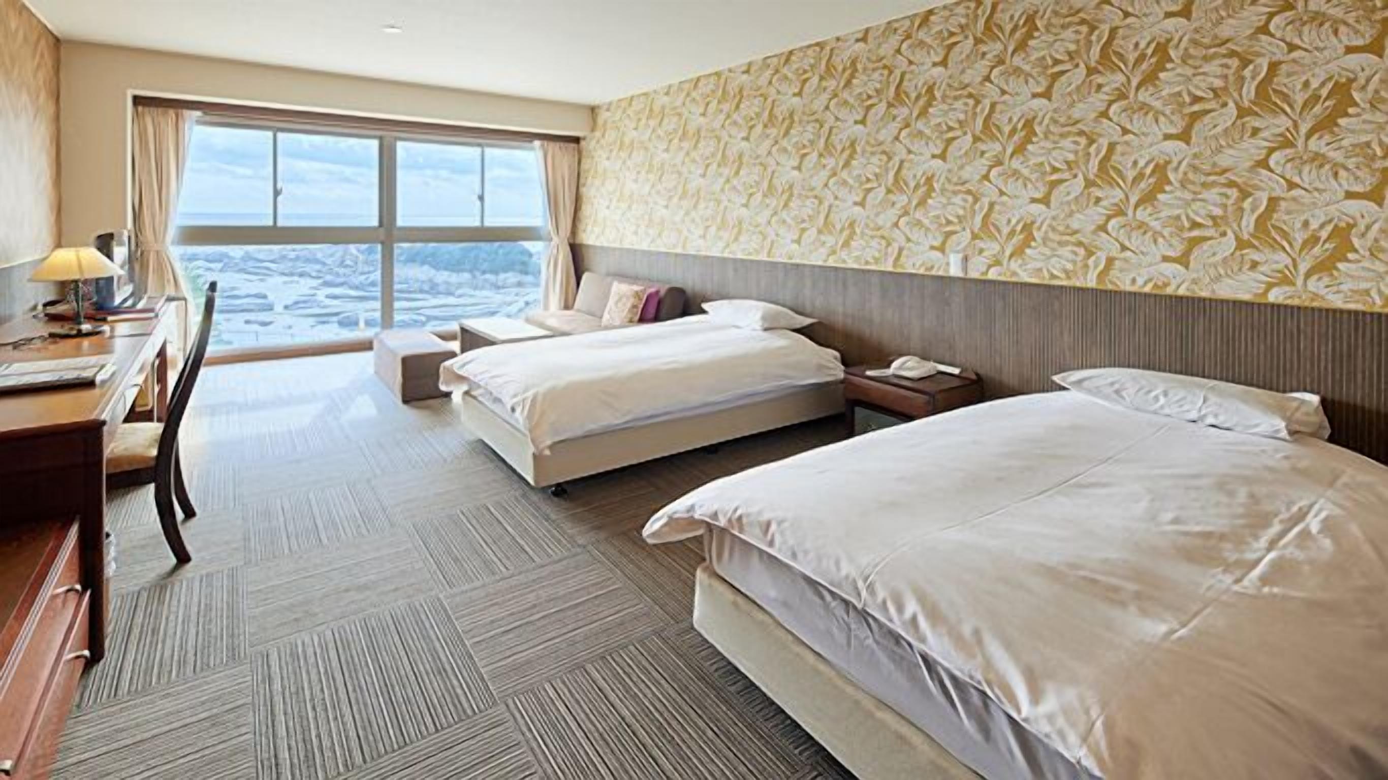 A hotel room with two beds, a desk, a chair, and a large window with a view.