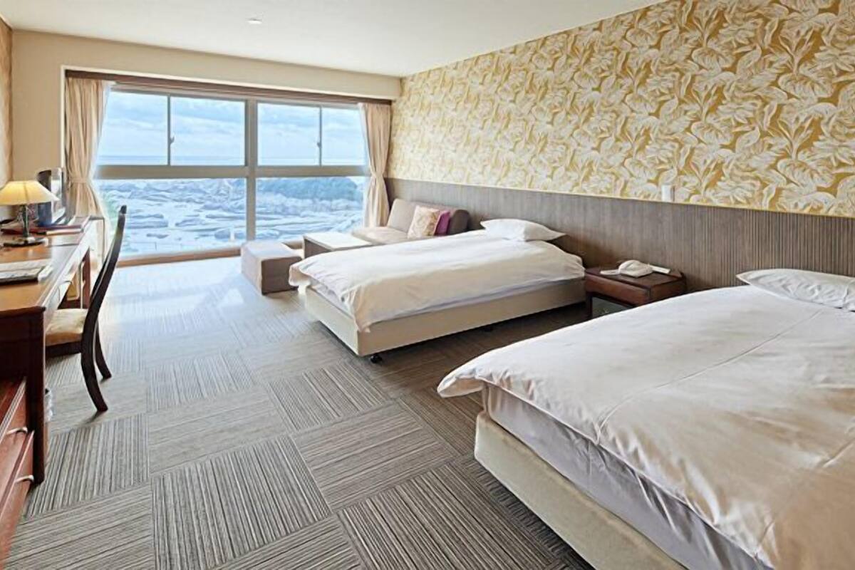 A hotel room with two beds, a desk, a chair, and a large window with a view.