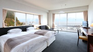 Une chambre d’hôtel avec deux lits, un bureau, une chaise et de grandes fenêtres donnant sur la mer.
