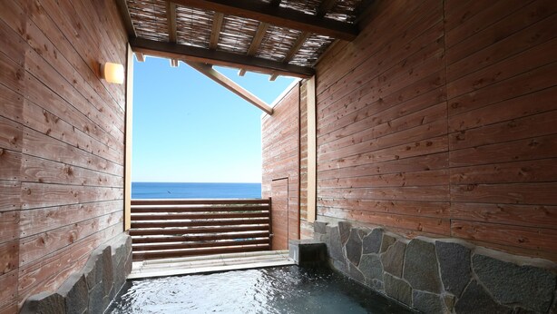 Un spa en bois avec un mur en pierre et une terrasse en bois donnant sur la mer.