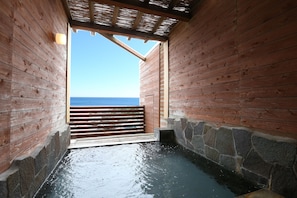 Un spa en bois avec un mur en pierre et une terrasse en bois donnant sur la mer.