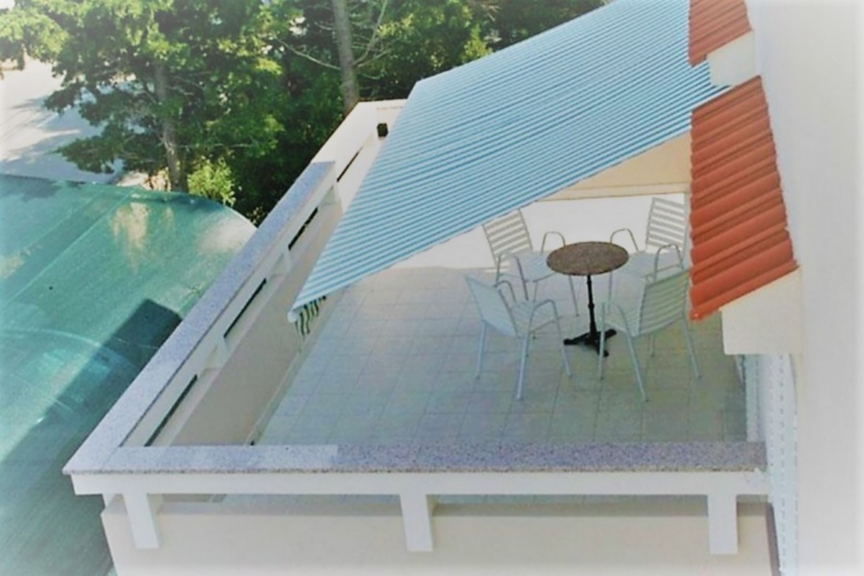 A rooftop terrace with a glass table and chairs, surrounded by a white railing.