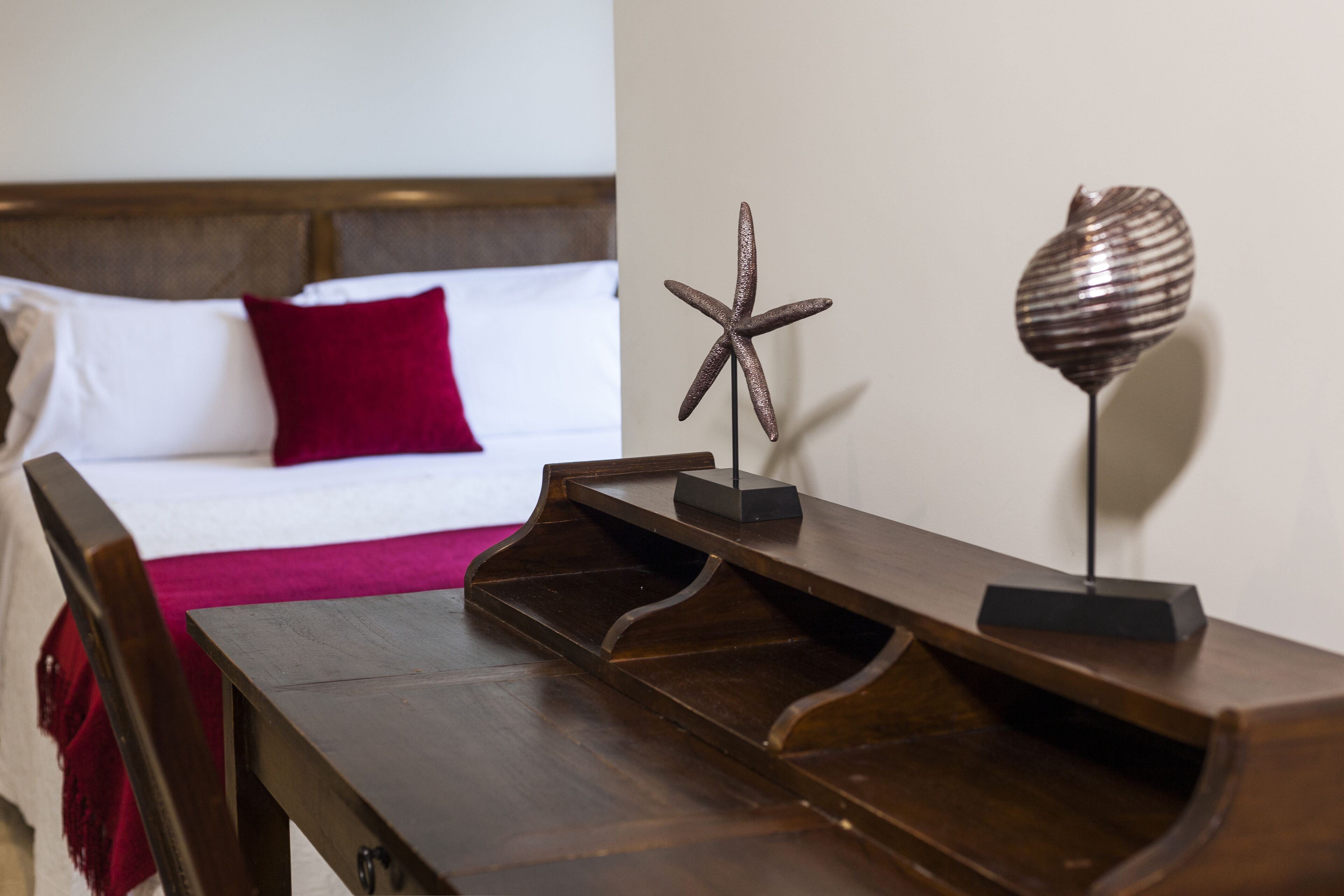 Una mesita de noche de madera con una decoración de estrella de mar y una lámpara, una cama con almohadas blancas y rojas, y un cabecero de madera.