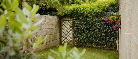 Un jardín con muro de piedra, cerca de madera y diversas plantas y flores.