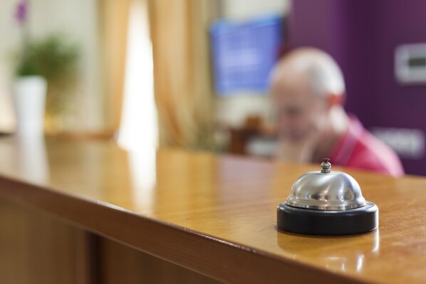A wooden reception desk with a silver bell and a black base.