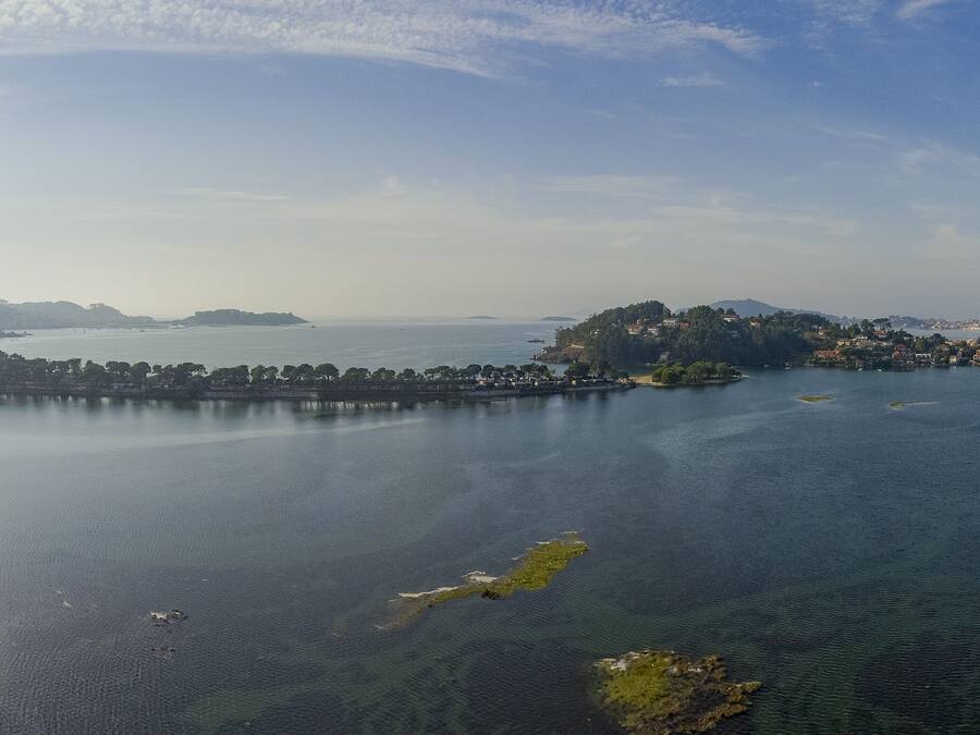A panoramic view of a coastal city with a large body of water, several islands, and a distant mountain range.