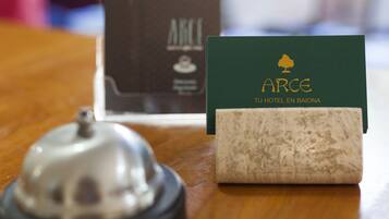 A hotel room with a wooden table, a bell, and a green card with the hotel name.