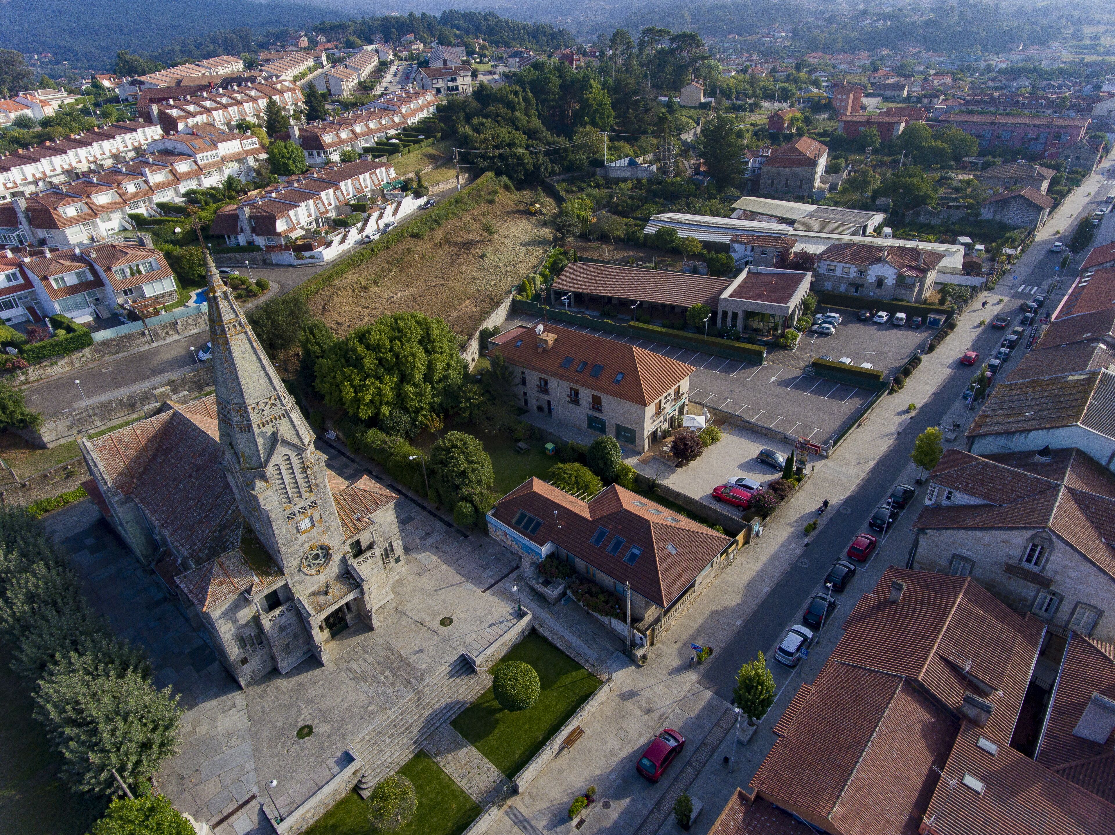 Vista aérea de um bairro residencial com casas em socalcos, uma igreja e um estacionamento.