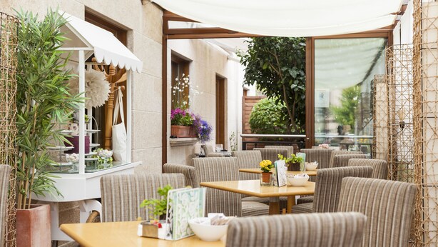 An outdoor cafe with wicker furniture, potted plants, and a white awning.