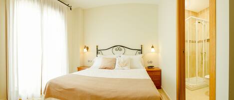 Un dormitorio con cama, mesitas de noche, candelabro y zona de ducha.