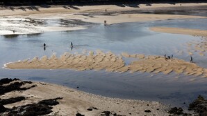 A beach with clear water, rocky areas, and people walking.