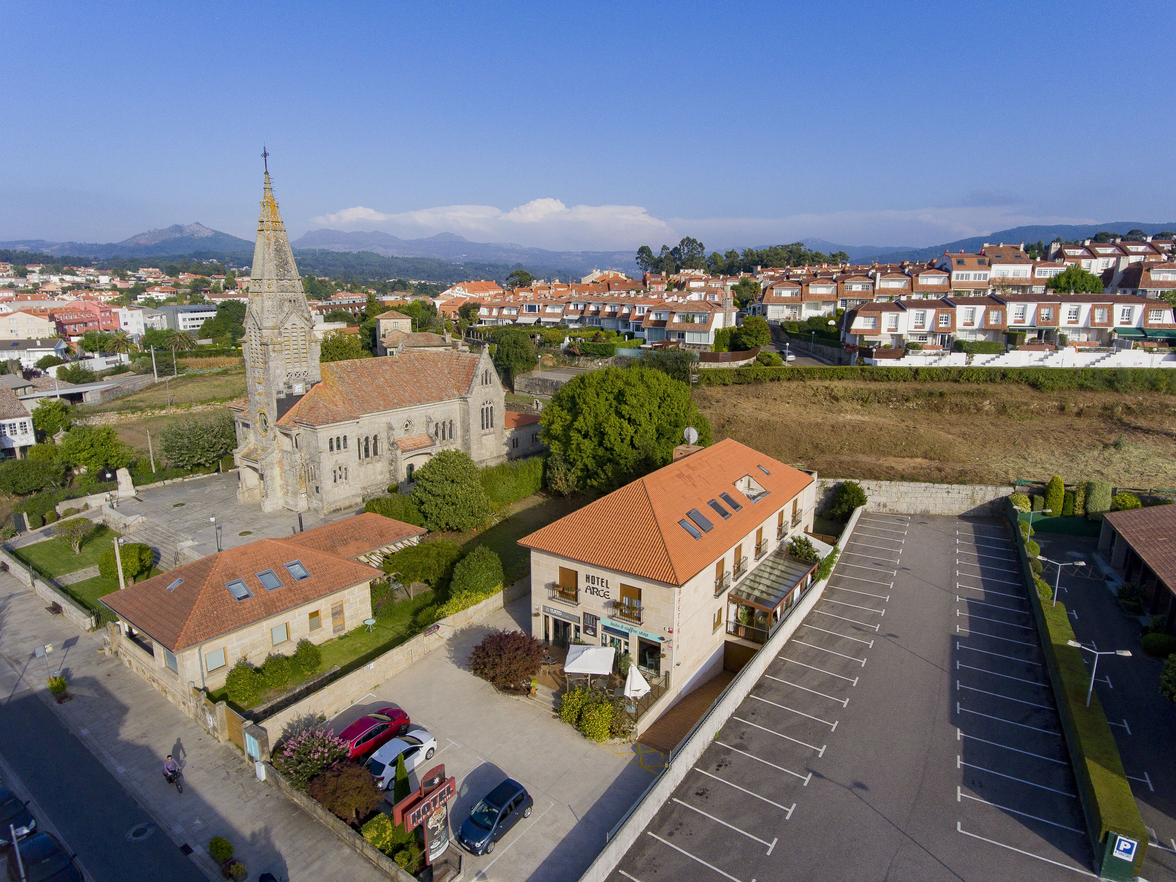 Vista aérea de un pueblo con una iglesia destacada, un hotel y un estacionamiento.