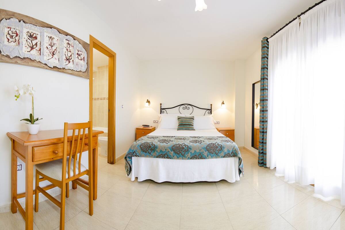 Um quarto com cama, mesas de cabeceira, escrivaninha e uma cadeira.