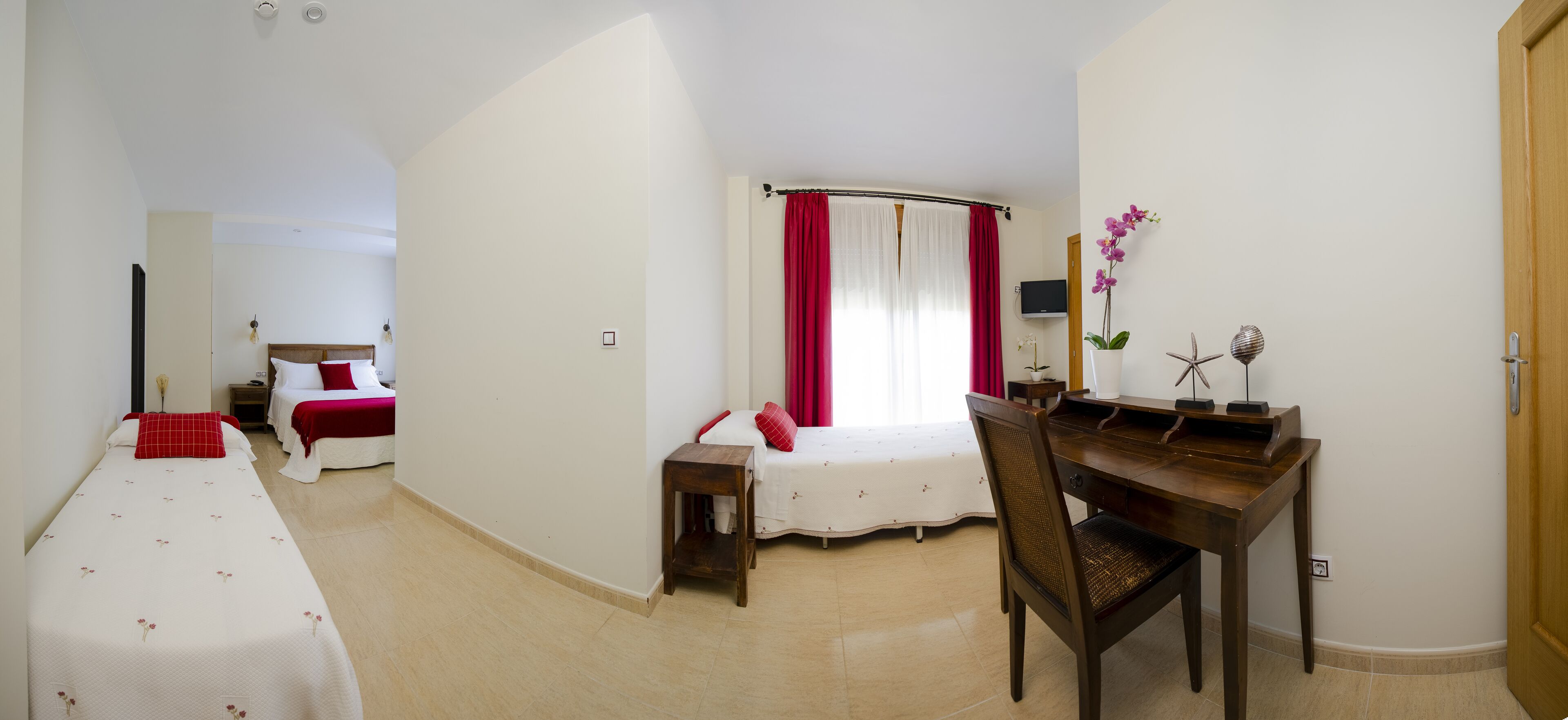 A hotel room with a bed, a desk, a chair, a small table, and a window with curtains.
