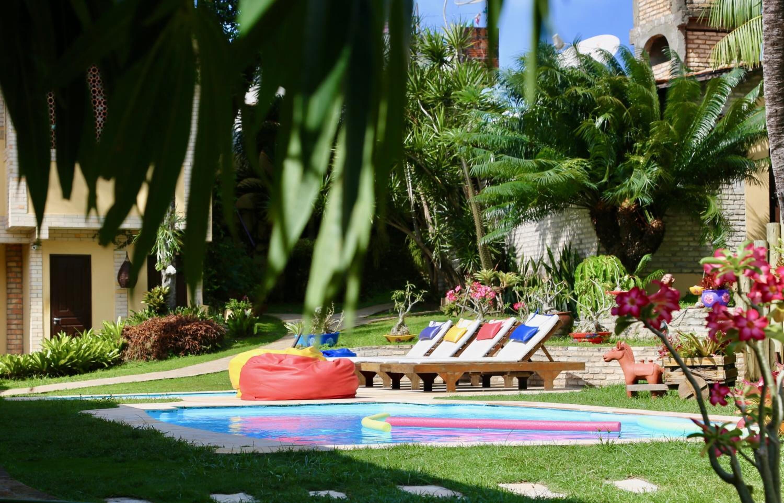 Un espace piscine aménagé avec des chaises longues, un fauteuil en forme de sac de haricots rouge et diverses plantes.