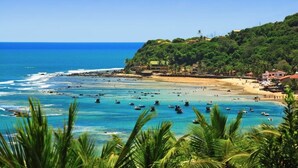 A coastal beach scene with boats, clear blue water, and a hillside with buildings. - Pousada Oasis (Tibau do Sul)