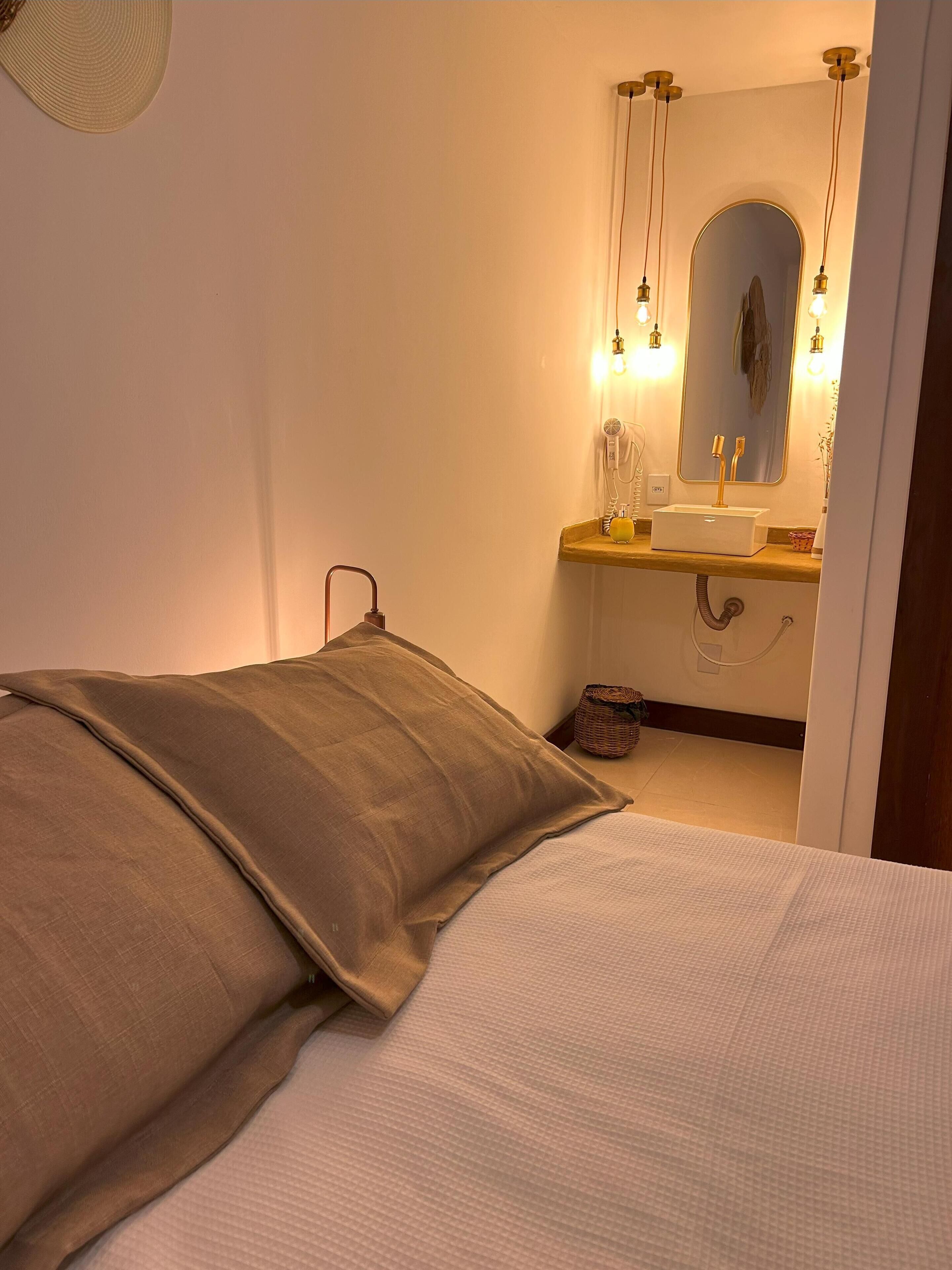 A bedroom with a bed, pillows, a bedside table, a mirror, and a sink with a towel hanging on the wall.