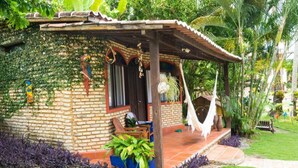 A rustic brick house with a covered porch, surrounded by lush greenery and a hammock. - Pousada Oasis (Tibau do Sul)