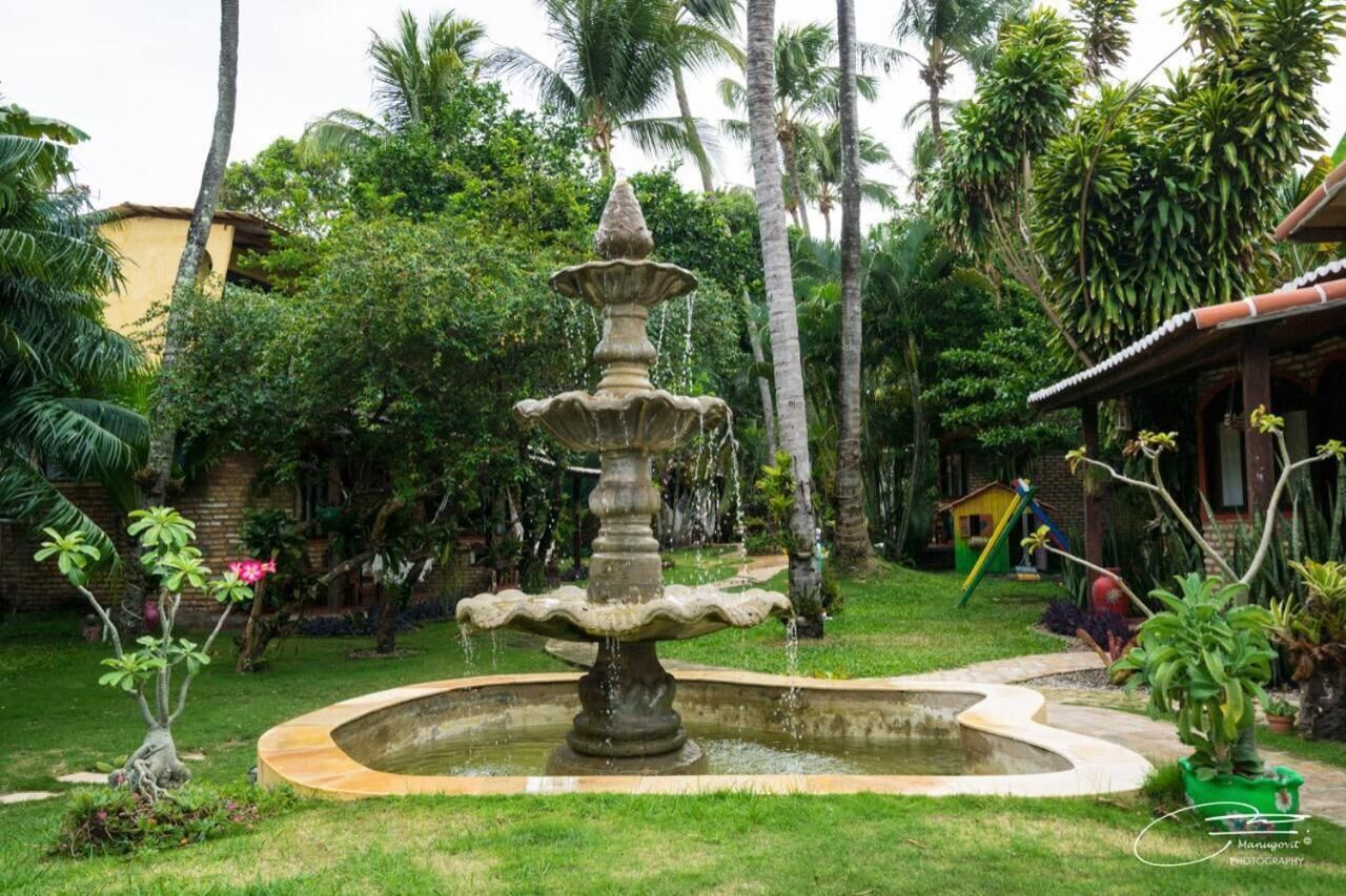 Un jardín con una fuente de piedra, rodeado de abundante vegetación y palmeras.