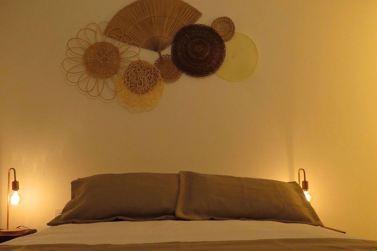 A bedroom with a bed, two bedside lamps, and a wall decoration above the bed.