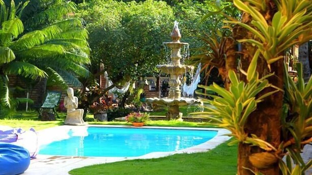 A reception sign for Pousada Oasis with a pool and lush greenery in the background. - Pousada Oasis (Tibau do Sul)
