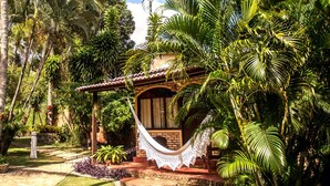 A tropical garden with a hammock, palm trees, and a brick building. - Pousada Oasis (Tibau do Sul)