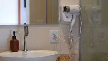 Une salle de bain avec un lavabo blanc, un miroir, un sèche-cheveux et un espace douche.