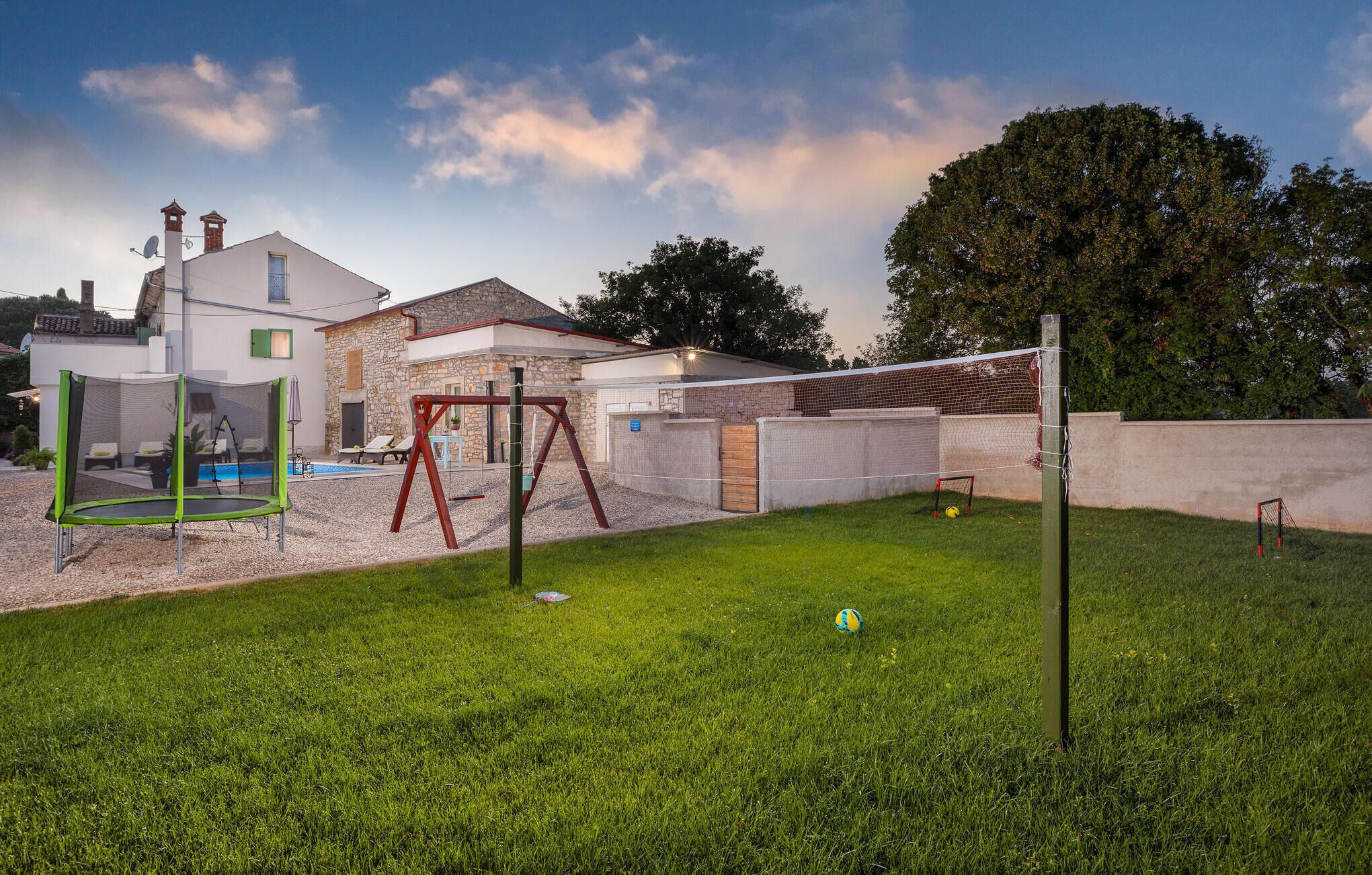A backyard with a trampoline, a swing set, a pool, and a soccer goal.