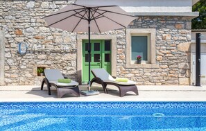 A stone building with a pool, two lounge chairs, a green door, and a window with a potted plant. - Lovely home in Duga Uvala (Duga Uvala)