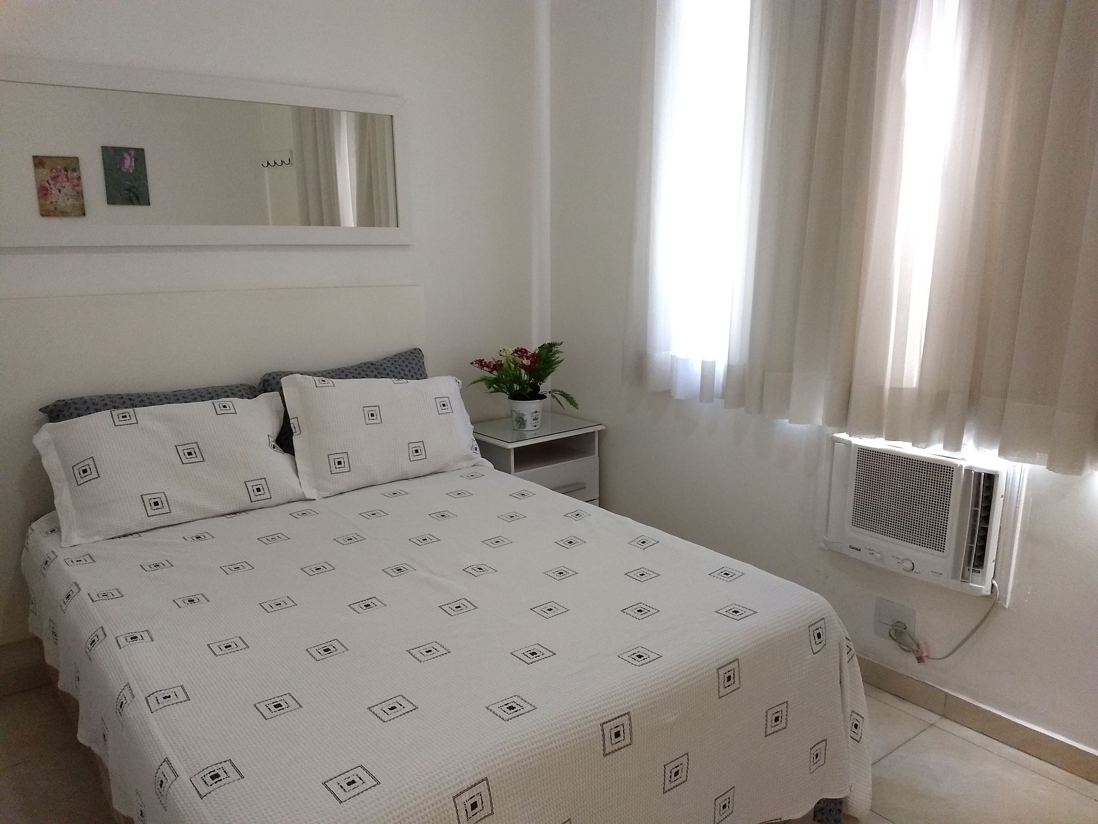 A neatly arranged bedroom with a bed, a bedside table with a potted plant, and a window with curtains.