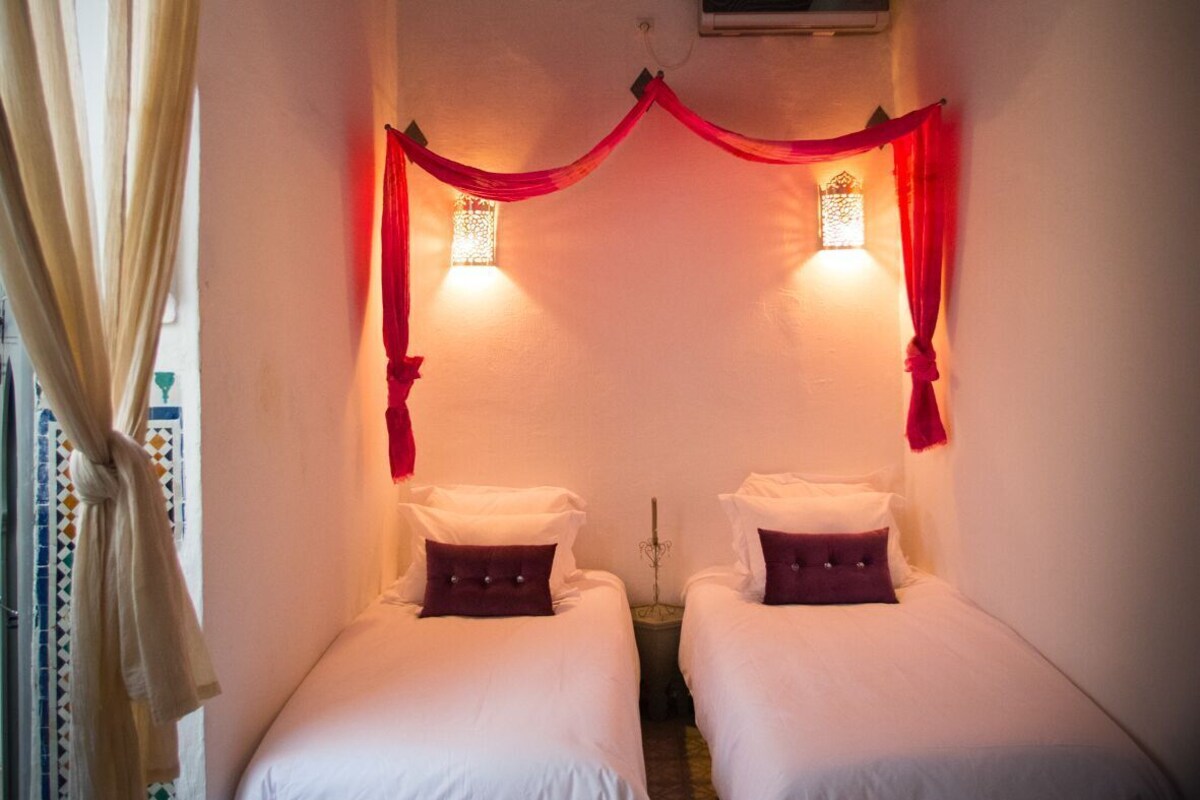 Una habitación con dos camas, una cortina decorativa roja y una lámpara colgante.