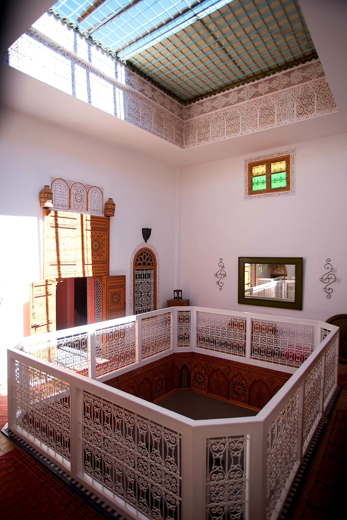 A room with intricate white lattice railings, a large ornate wooden door, and a small window with green-tinted glass.