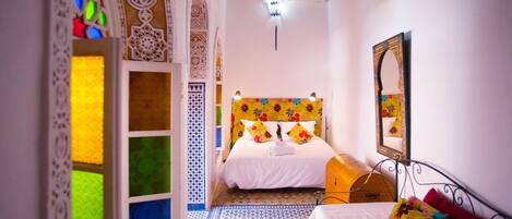 A room with a bed, a small table, a mirror, and a patterned floor.