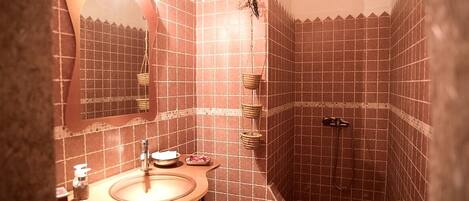 A bathroom with a sink, mirror, and a shower area with tiled walls.