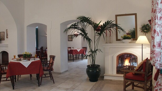 A dining area with tables set for two, a large potted plant, and a fireplace with a lit fire. - Golf Club Metaponto (Bernalda)