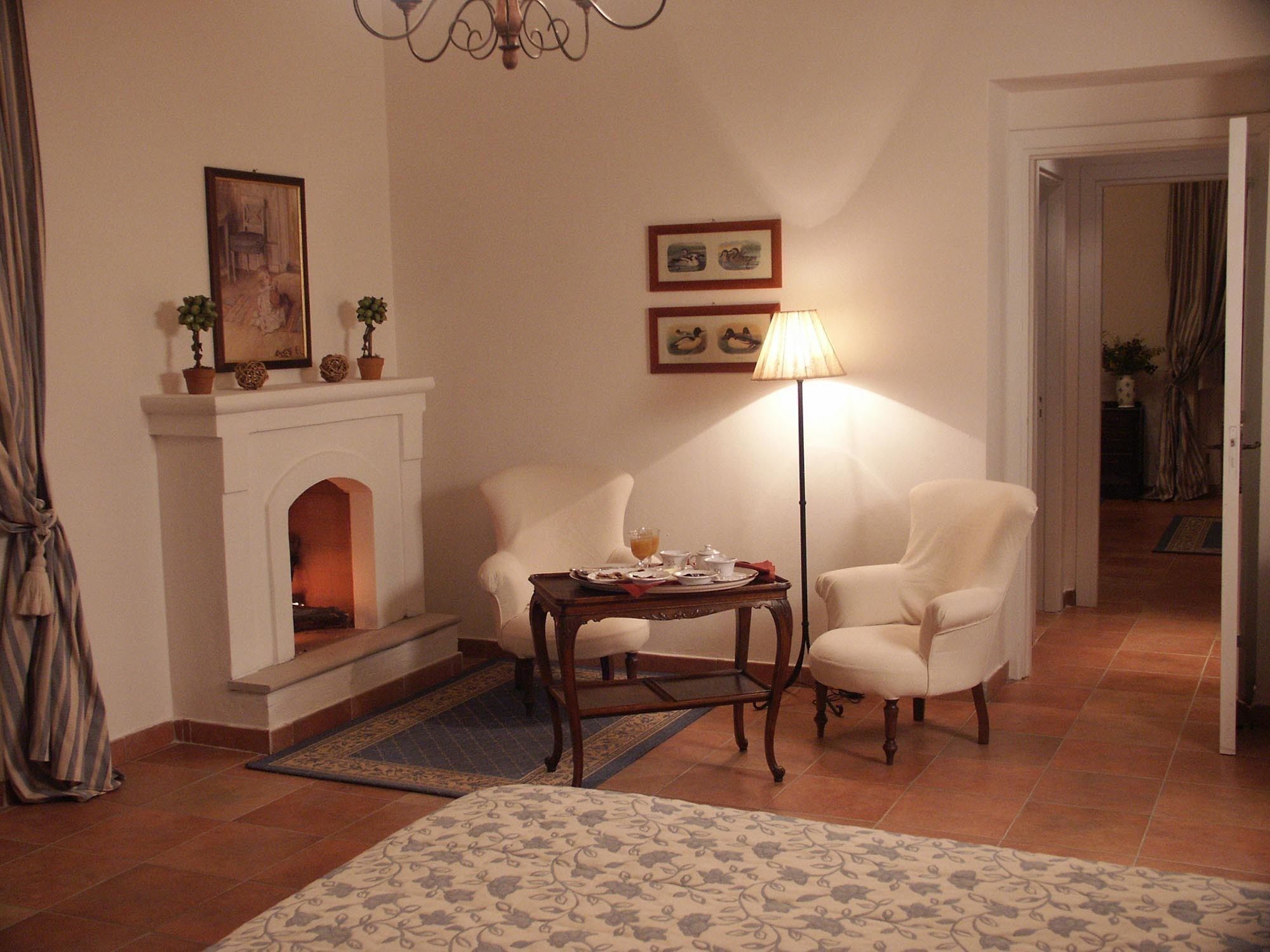 Una habitación con chimenea, dos sillones, una mesita con lámpara y una alfombra estampada.