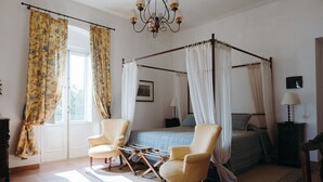 A four-poster canopy bed with a blue and white checkered bedspread, two armchairs, a nightstand with a lamp, and a chandelier. - Golf Club Metaponto (Bernalda)