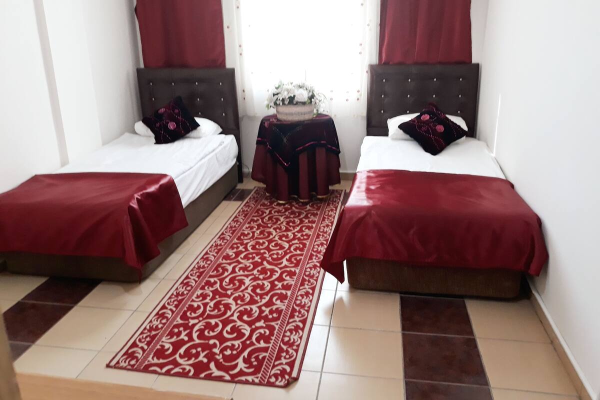 A hotel room with two beds, a red carpet, and a small table with a vase of flowers.
