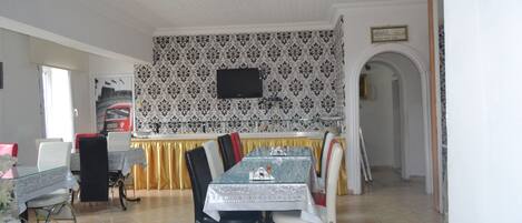Comedor con una mesa lista para cuatro personas, un televisor montado en la pared y un diseño de papel tapiz estampado.