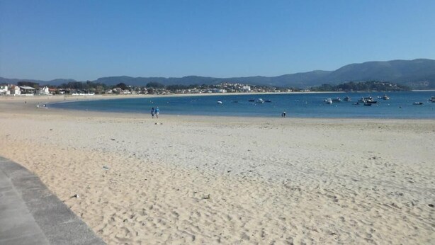 Ein Strand mit klarem Himmel, ruhiger See und fernen Bergen.