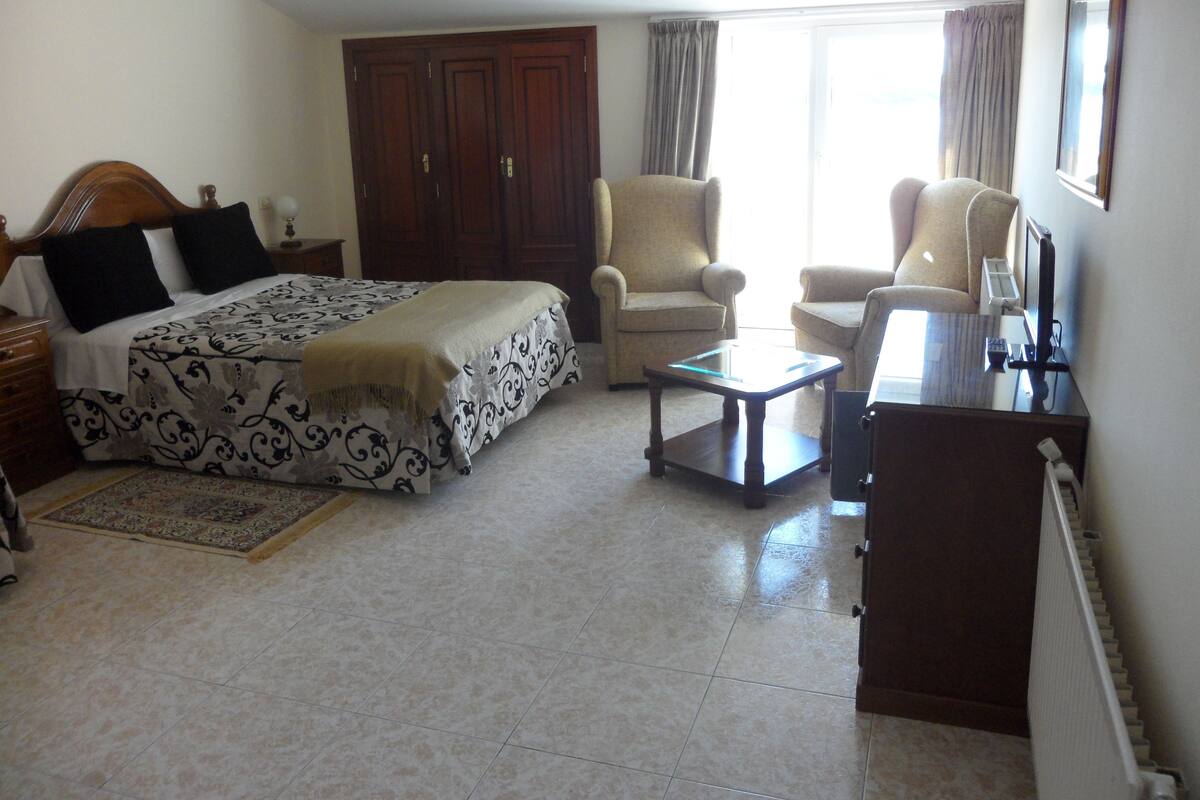 A bedroom with a bed, two chairs, a desk, and a wardrobe.