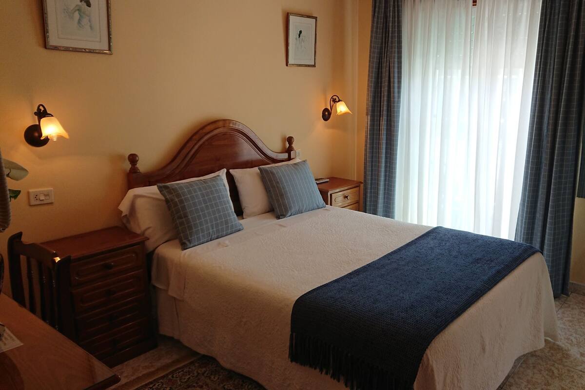 A hotel room with a large bed, two bedside tables, a television, and a window with curtains.