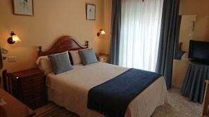 A hotel room with a large bed, two bedside tables, a television, and a window with curtains. - Hotel Avenida (Baiona)