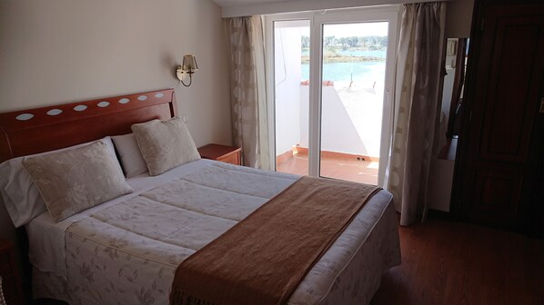 A hotel room with a bed, a nightstand, a wall-mounted lamp, and a view of a pool through a sliding glass door. - Hotel Avenida (Baiona)