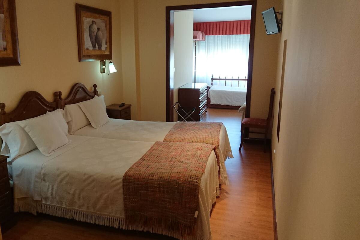 A double bed with a wooden headboard, a bedside table, and a nightstand. There is a door leading to a balcony with a view of the outside.