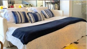 A neatly made bed with a white and blue striped duvet, a dark blue throw blanket, and multiple pillows. - Copa Loft (Rio de Janeiro)