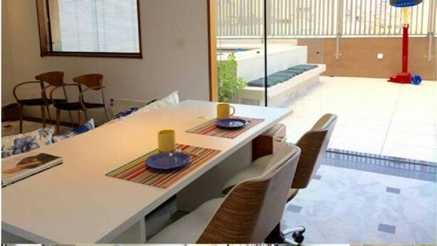 A dining area with a long table, chairs, and a view of a balcony with a railing and a basketball hoop. - Copa Loft (Rio de Janeiro)